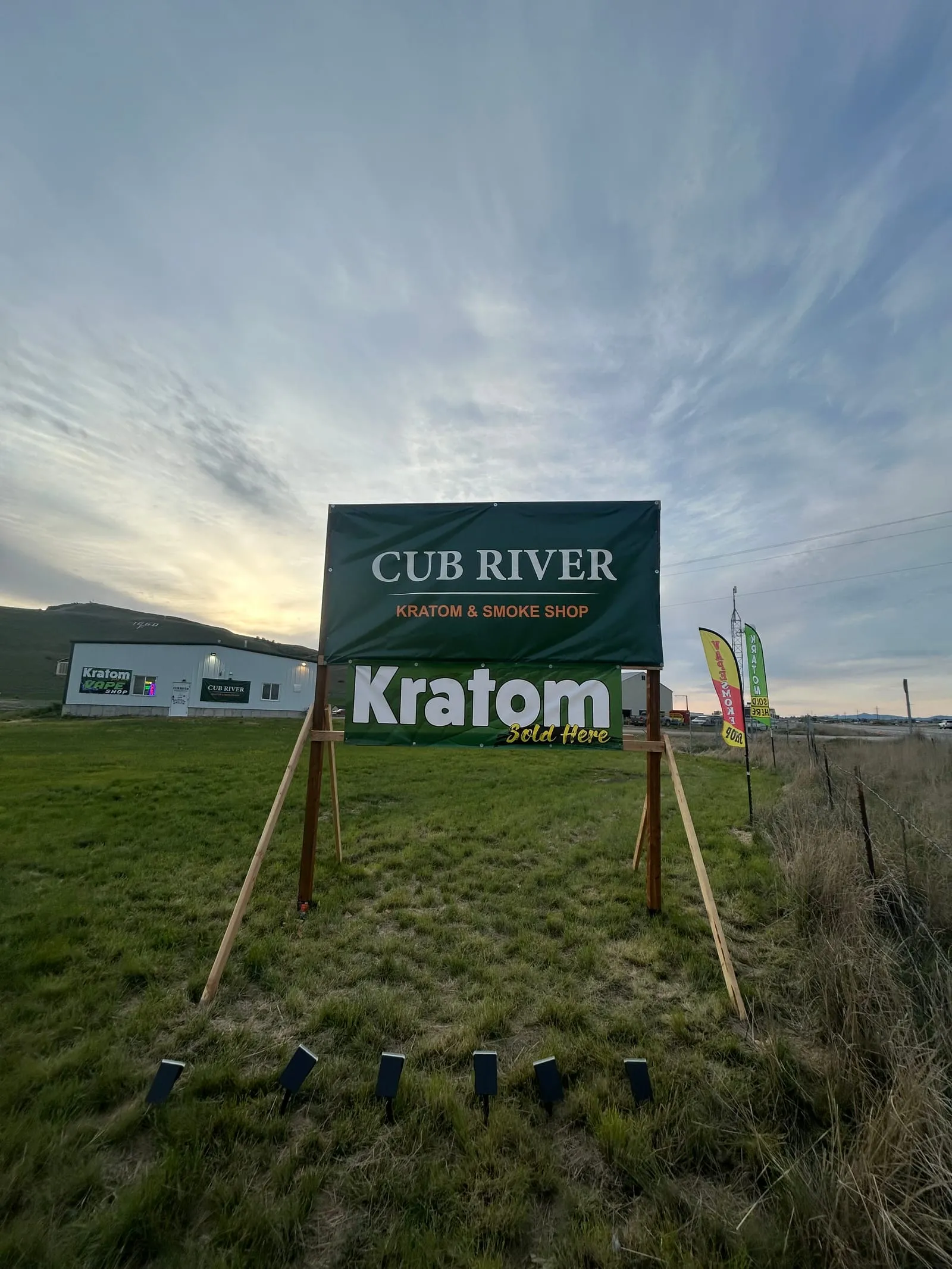 Cub River Kratom & Vape Shop storefront sign reading "Kratom Sold Here" against an evening sky